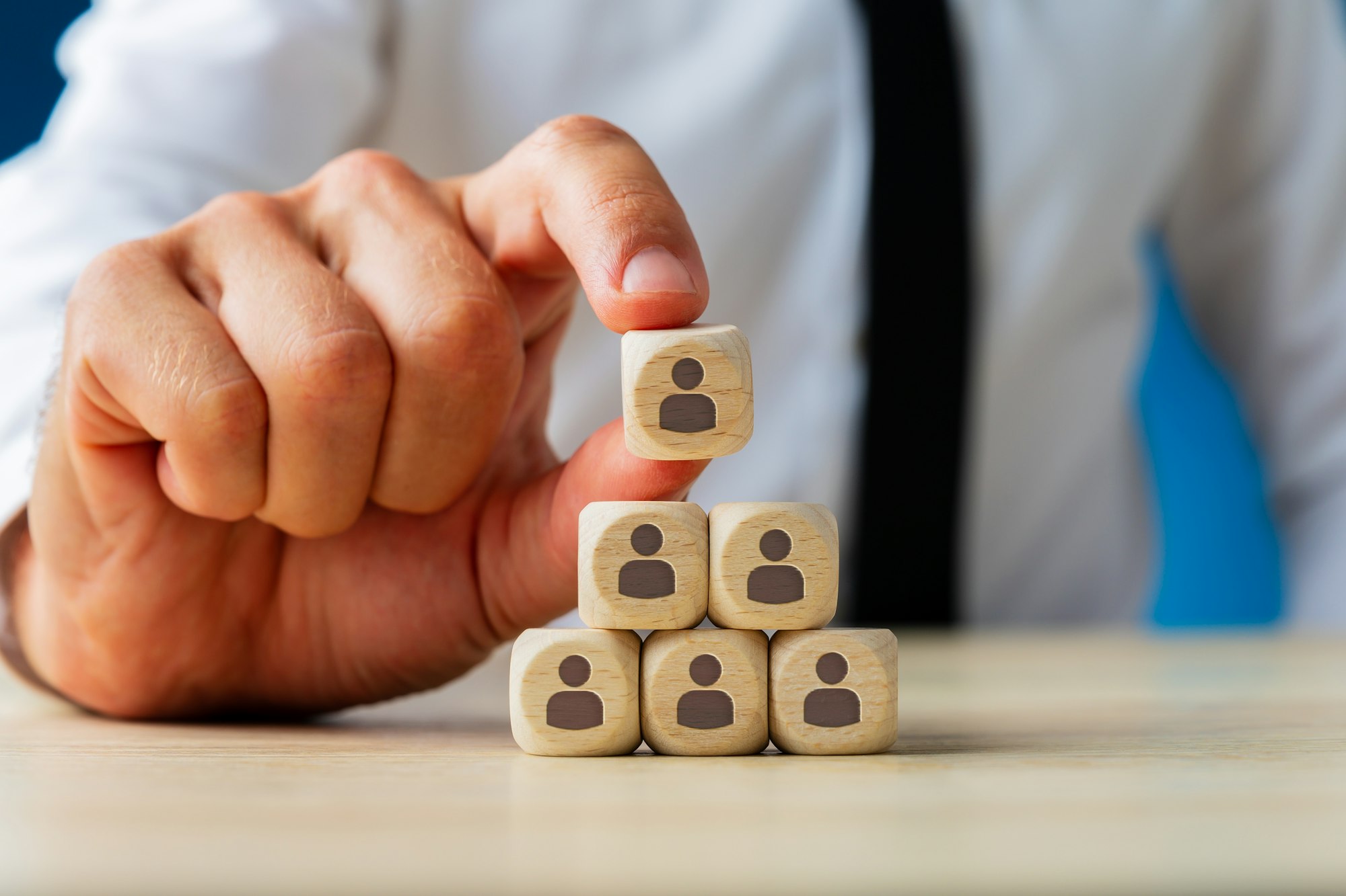 Business executive stacking wooden dices with people icons on them in a pyramid shape